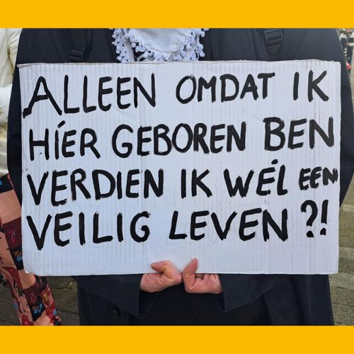 Persoon houdt een protestbord vast met de tekst:

'Alleen omdat ik híer geboren ben verdien ik wél een veilig leven?!'
