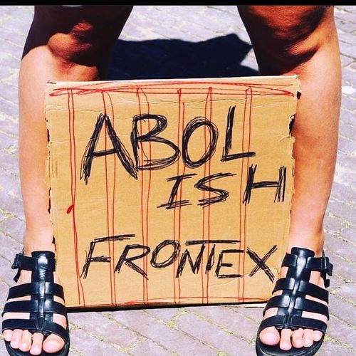 Picture from someone standing on the street with a cardboard banner saying 'ABOLISH FRONTEX' standing on the ground between their feet.